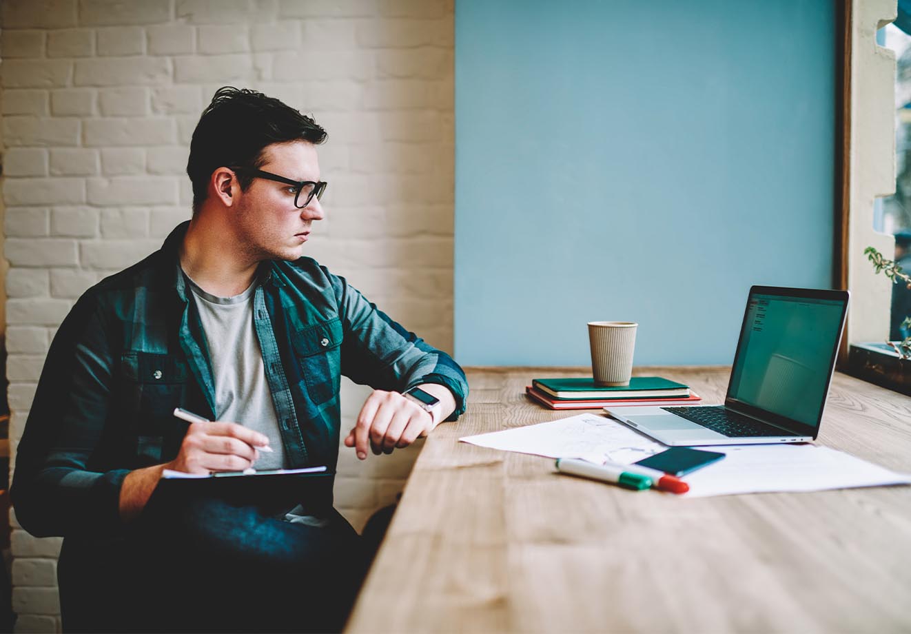 Man writing on a clipboard while looking at a laptop