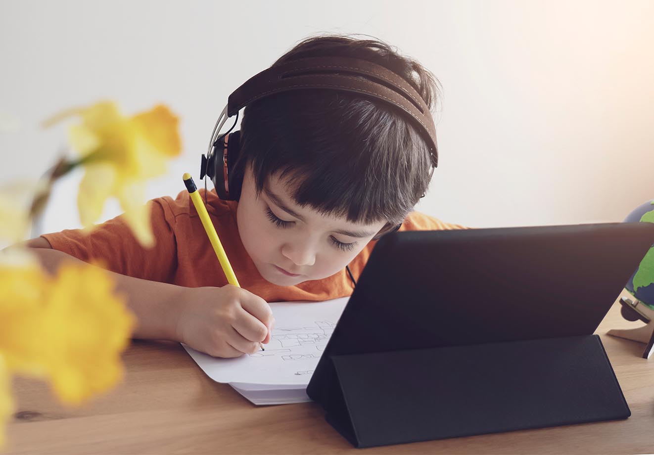A child studies at a computer while taking notes.