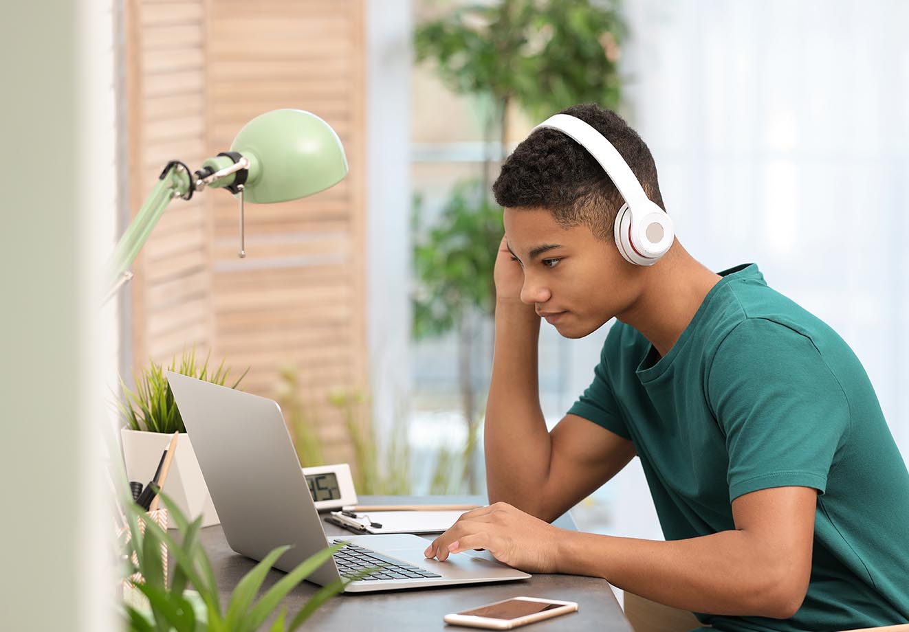 A student sits at a laptop listening with wireless headphones.