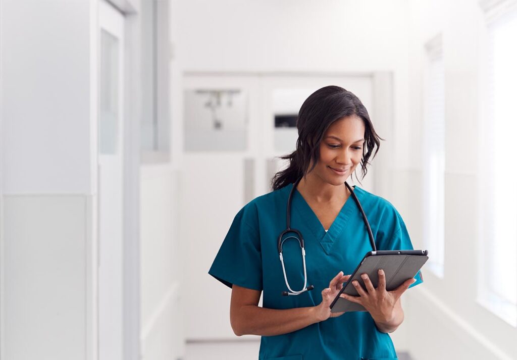 A healthcare professional walking in a hallway looking at a tablet
