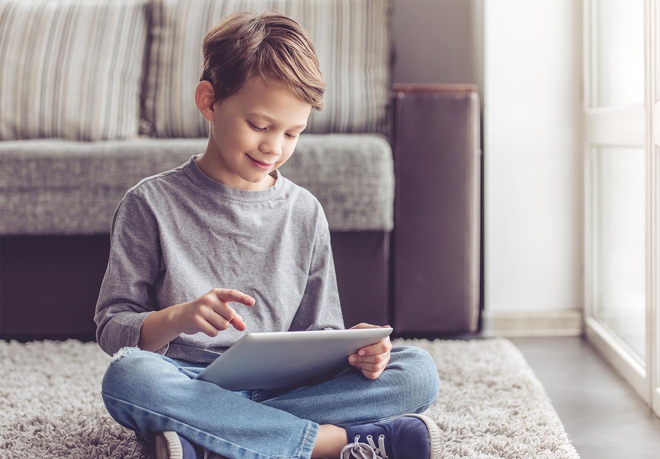 young boy sitting cross-legged on the floor and looking at a tablet in his lap
