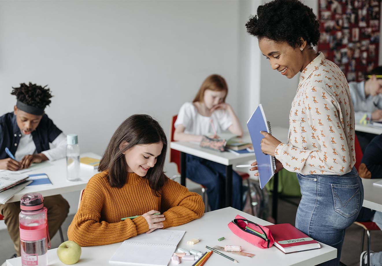 A teacher checks in on a student at a desk.