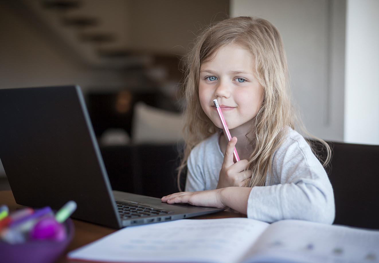 young girl working on a laptop and holding a pencil in one hand