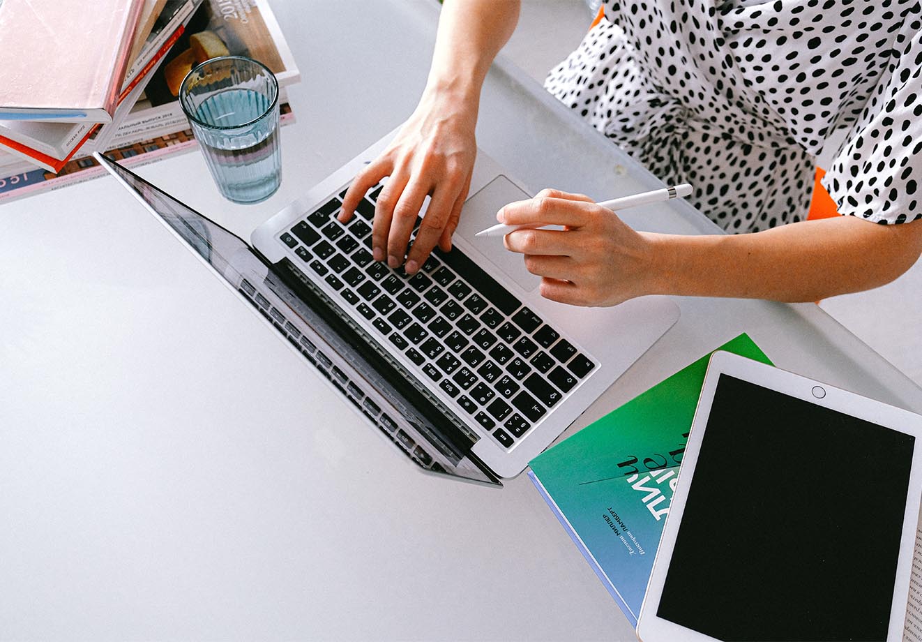 A person types on a computer with a pen in-hand