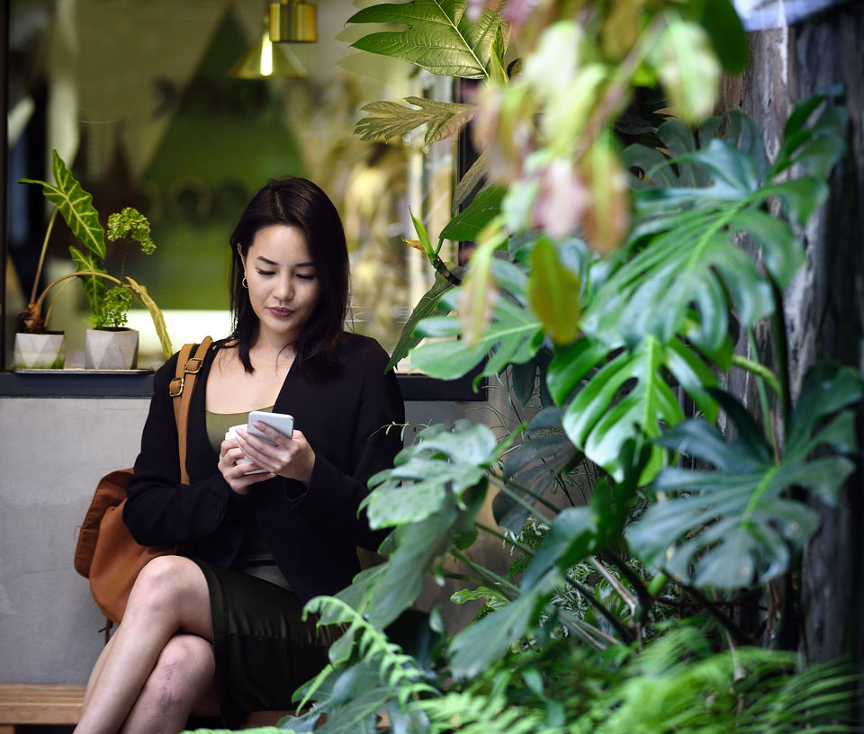 Woman on phone sitting on a bench with plants around