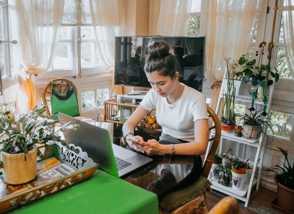 Woman on phone in front of computer with plants around