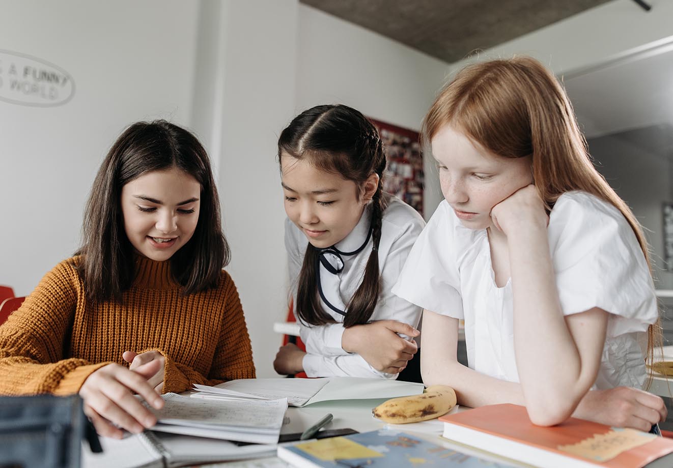 three young students lean over a busy desk, looking at an ipad