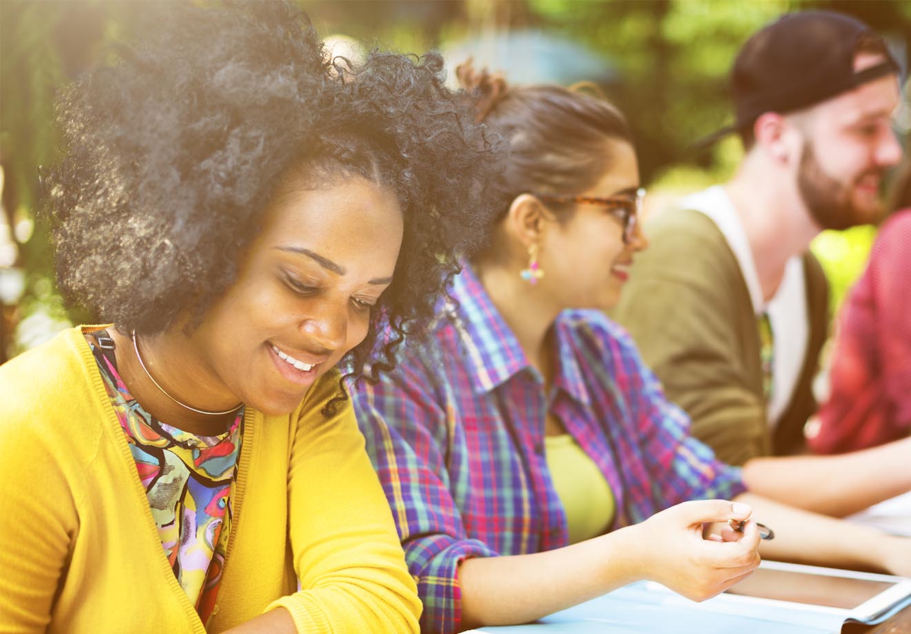 Three higher ed students sit in a row, studying, off campus and outdoors.
