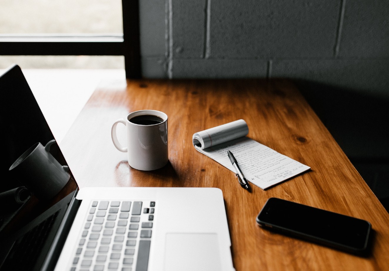 Laptop, coffee, phone, and notepad on a desk
