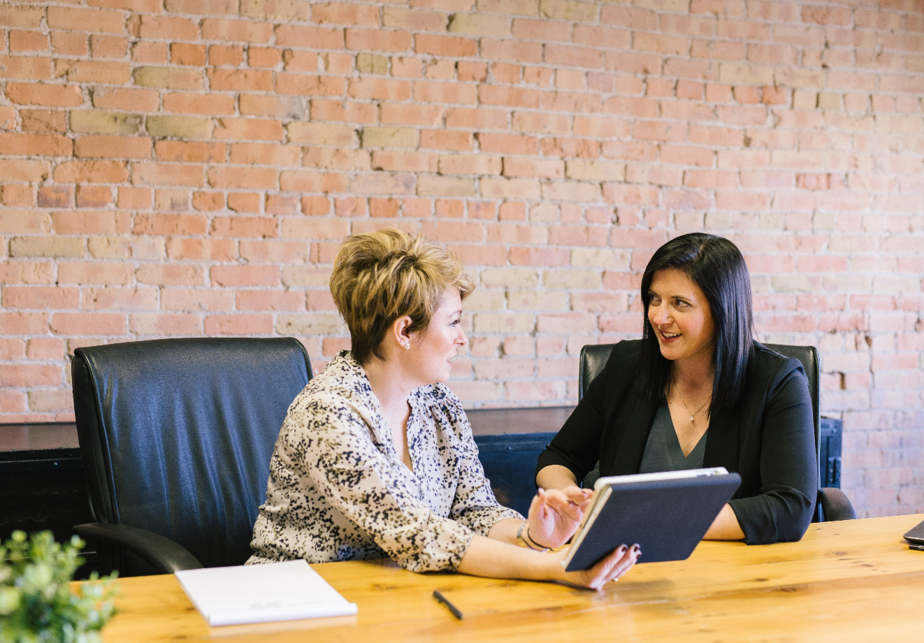 Two colleagues sit side by side at a desk consulting a tablet