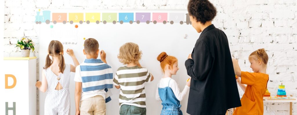 The children stood in a line and drew on the wall while the teacher watched from behind