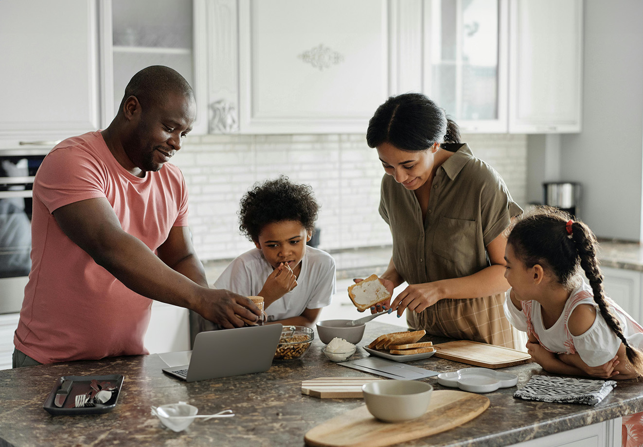 A family of four gathered around granite table in kitchen, preparing food together